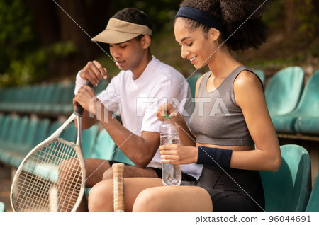 Two tennis players resting after the game and looking contented Two tennis players resting after the game and looking contented 96044691