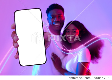 Happy black lovers hugging and showing smartphone with empty screen Happy black lovers hugging and showing smartphone with empty screen 96044792