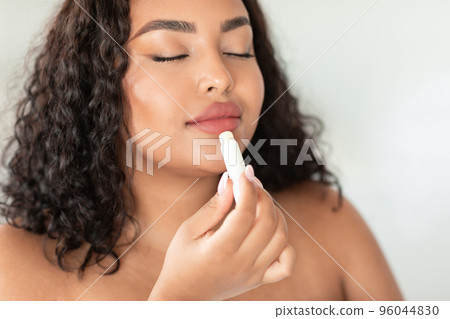 Lip care concept. Beautiful african american plus size woman using chapstick to moisturise her plump lips 96044830