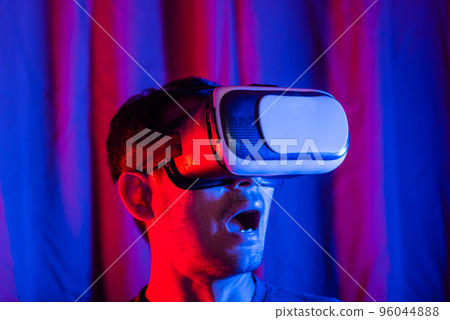 Asian handsome man wear VR helmet excited emotional at home purple and blue background, experiencing virtual reality goggles experiencing reality excited emotional, metaverse and cyberspace 96044888