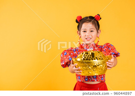 Chinese New Year. Happy Asian Chinese little girl smile wearing red cheongsam holding big gold ingot, Portrait children in traditional dress hold golden bar, studio short isolated on yellow background Chinese New Year. Happy Asian Chinese little girl smile wearing red cheongsam holding big gold ingot, Portrait children in traditional dress hold golden bar, studio short isolated on yellow background 96044897