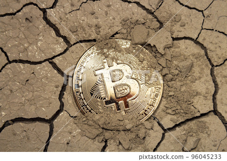 Golden bitcoin in the form of a coin lies on dry cracked ground 96045233