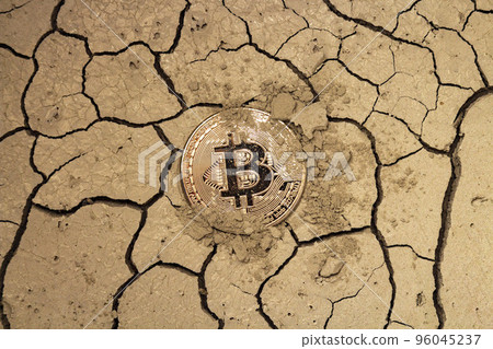 Golden bitcoin in the form of a coin lies on dry cracked ground 96045237