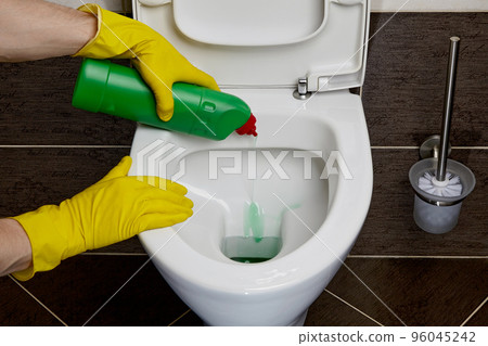 Hands in yellow rubber gloves pour disinfectant into the toilet 96045242