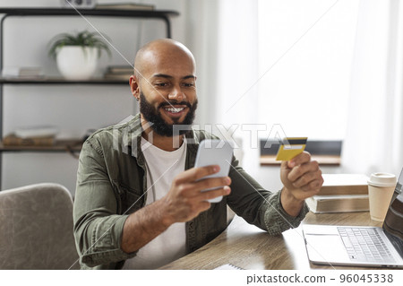 Buy and pay at home. Happy mature latin man using smartphone and credit card, shopping online, sitting at desk at home 96045338
