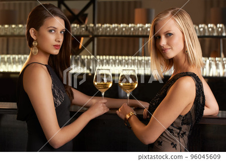 Evening style. Shot of two women standing at a bar in evening wear. 96045609