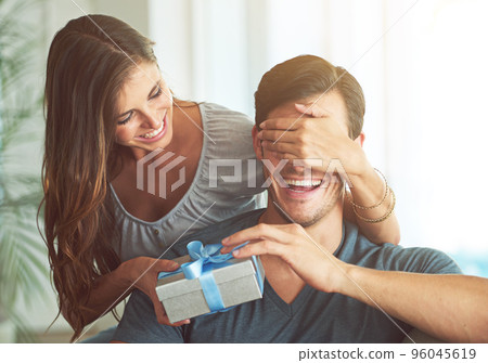 I got you something, honey. A young woman covering her husbands eyes for a surprise gift. 96045619