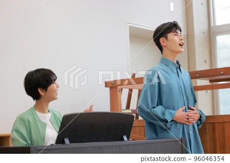 A voice trainer teaching while playing the piano and a man practicing vocalization_1 96046354