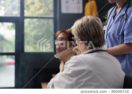 Medical staff taking cervical neck collar off of injured asian woman with physical trauma, rehabilitation therapy and recovery in hospital waiting area. Patient receiving medicine support 96046538