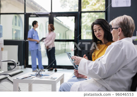 Asian patient looking at medical radiography with senior doctor discussing illness diagnosis during consultation in hospital waiting area. Women talking about healthcare service support 96046553