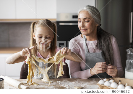 Cheerful caucasian little granddaughter and elderly grandmother make cookie dough, enjoy lesson 96046622