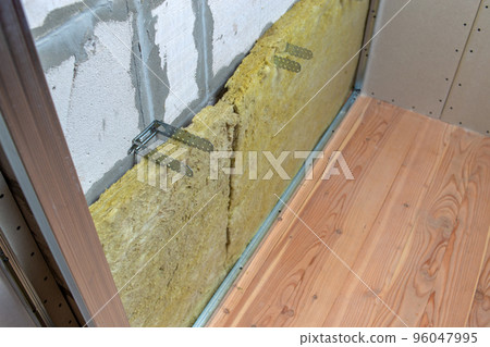 Wall of a room under renovation with mineral rock wool insulation and metal frame prepared for drywall plates. 96047995