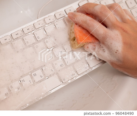 Woman washing white computer keyboard with a sponge with foam. 96048490