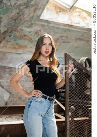 Woman in jeans and black t-shirt posing near wire fencing in abandoned factory 96052130