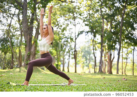 Healthy Asian woman practicing High Lunge Crescent pose or warrior I pose in the garden. 96052453