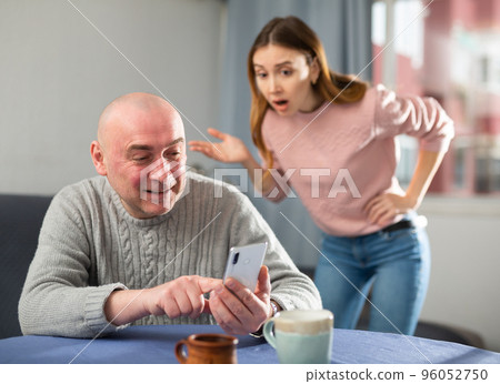 Man is texting on a mobile phone, while woman is outraged 96052750
