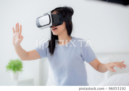 Young asian woman wearing vr headset playing game with excited on bed in the bedroom. 96053192