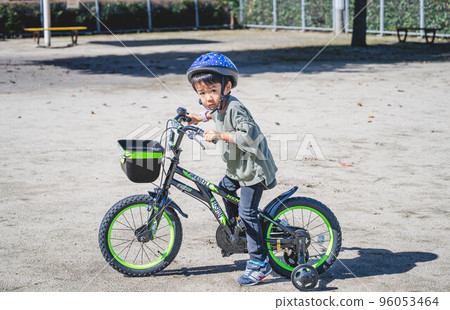 一個孩子戴著頭盔騎著帶訓練輪的自行車 96053464