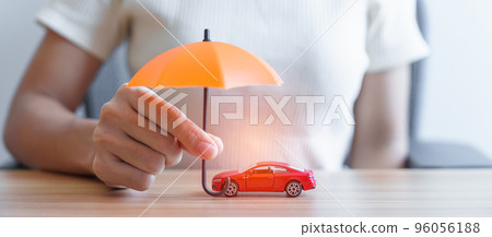 Businesswoman hand holding orange umbrella and cover red car toy on table. Car insurance, warranty, repair, Financial, banking and money concept Businesswoman hand holding orange umbrella and cover red car toy on table. Car insurance, warranty, repair, Financial, banking and money concept 96056188