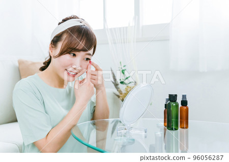 A woman looking in the mirror with a smile at home (eyes / contact lenses) 96056287