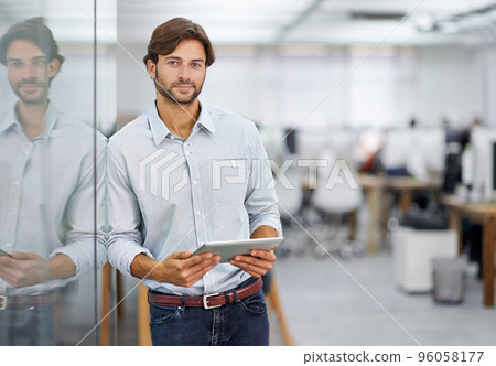 Hes a confident young businessman. Portrait of a handsome young businessman standing in his office. 96058177
