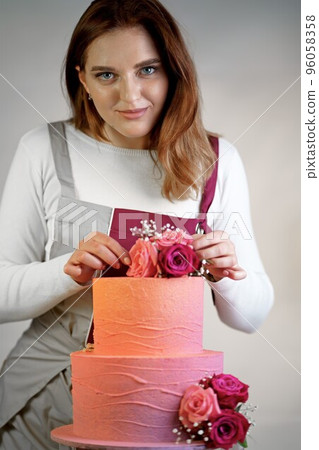 Beautiful girl confectioner in a working apron decorates a birthday cake with fresh flowers 96058358