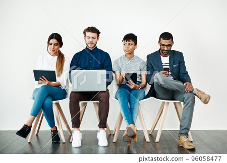 Enjoying instant notifications and endless apps. Shot of a group of young people using wireless technology while sitting in a row. 96058477
