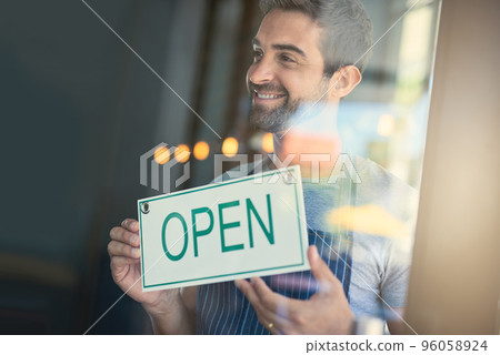 Time to serve some awesome coffee. Shot of a handsome young man hanging up an open sign on the door of his store. Time to serve some awesome coffee. Shot of a handsome young man hanging up an open sign on the door of his store. 96058924