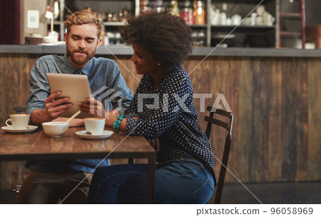 Showing him an interesting clip online. Shot of a young couple using a digital tablet together on a coffee date. Showing him an interesting clip online. Shot of a young couple using a digital tablet together on a coffee date. 96058969