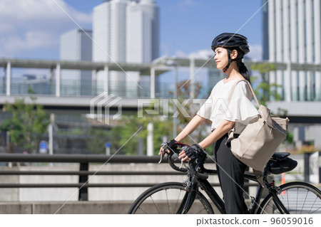 一位女商人肩上背著背包走路，從旁邊拉著一輛公路自行車 96059016