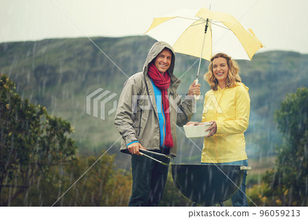 Come rain or shine. Shot of a couple happily barbecuing in the rain. Come rain or shine. Shot of a couple happily barbecuing in the rain. 96059213