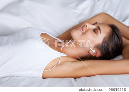 Musical escape.... Portrait of a beautiful young woman listening to music while lying on her bed. 96059238