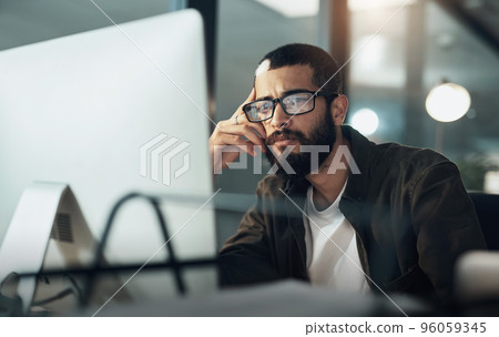 The later it gets the deeper he goes. Shot of a young businessman using a computer during a late night in a modern office. The later it gets the deeper he goes. Shot of a young businessman using a computer during a late night in a modern office. 96059345