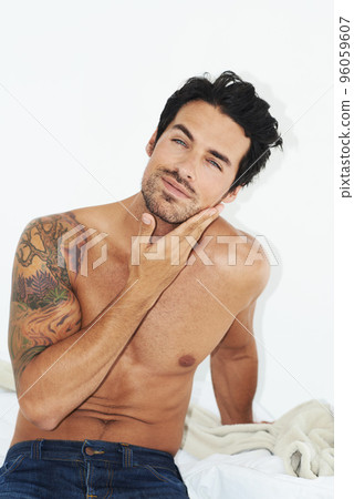 Waking up is a long process.... Shot of a handsome bare-chested man sitting on his bed and rubbing his chin. 96059607