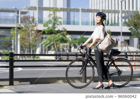 A business woman carrying a backpack and walking by pulling a road bike from the side 96060042