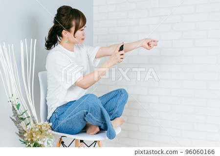 Smiling Japanese woman spraying her arm Smiling Japanese woman spraying her arm 96060166