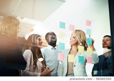 Marketers flexing their mental muscles. Shot of a group of businesspeople arranging sticky notes on a glass wall in a modern office. Marketers flexing their mental muscles. Shot of a group of businesspeople arranging sticky notes on a glass wall in a modern office. 96060300