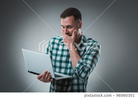 Frustrated businessman holding a laptop covers his face with his hand on gray background. Frustrated businessman holding a laptop covers his face with his hand on gray background. 96060301