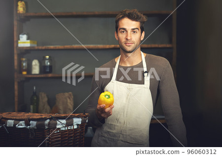 Hes a pro in the kitchen. Shot of a young man holding a yellow pepper in his kitchen. Hes a pro in the kitchen. Shot of a young man holding a yellow pepper in his kitchen. 96060312