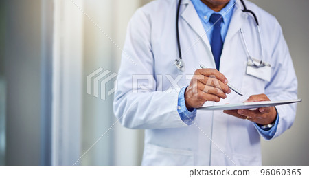 His schedules are always busy. Shot of an unrecognizable male doctor writing on a digital tablet while standing inside of a hospital during the day. His schedules are always busy. Shot of an unrecognizable male doctor writing on a digital tablet while standing inside of a hospital during the day. 96060365