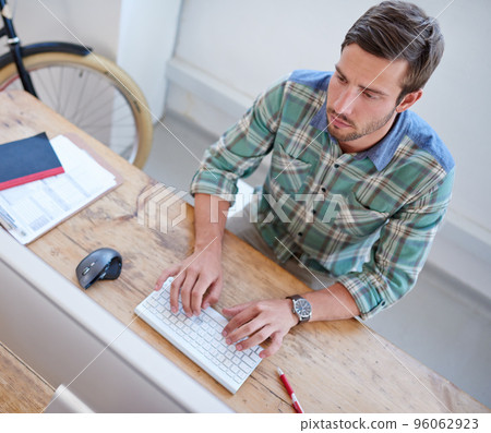 This is the hard work behind the dream. Top view of a handsome young man typing on his wireless keyboard at his desk in the office. This is the hard work behind the dream. Top view of a handsome young man typing on his wireless keyboard at his desk in the office. 96062923