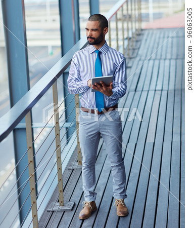 Technology brings business closer to him. Shot of a young businessman using a digital tablet outside of an office building. Technology brings business closer to him. Shot of a young businessman using a digital tablet outside of an office building. 96063005