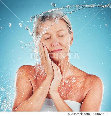 Senior woman, water and skincare for hydrate, hygiene and fresh clean treatment against a blue studio background. Happy elderly female touching face for smooth facial hydration or skin moisture 96063308