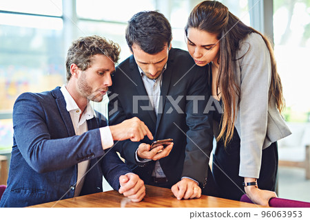 Lets enjoy connectivity together. Cropped shot of businesspeople using a cellphone together indoors. Lets enjoy connectivity together. Cropped shot of businesspeople using a cellphone together indoors. 96063953