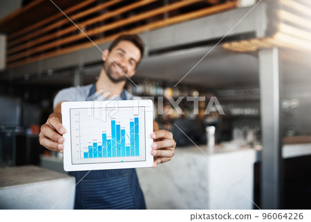 The figures have never looked this good. Portrait of a young man holding a digital tablet with a graph on the screen at a coffee shop. The figures have never looked this good. Portrait of a young man holding a digital tablet with a graph on the screen at a coffee shop. 96064226