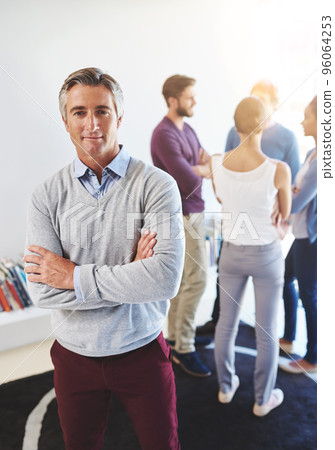 Hes a man with a plan. Portrait of a mature businessman with his colleagues standing in the background. Hes a man with a plan. Portrait of a mature businessman with his colleagues standing in the background. 96064253