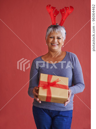 Heres a little something for you. Shot of a mature woman holding a gift and wearing festive reindeer antlers. 96064462