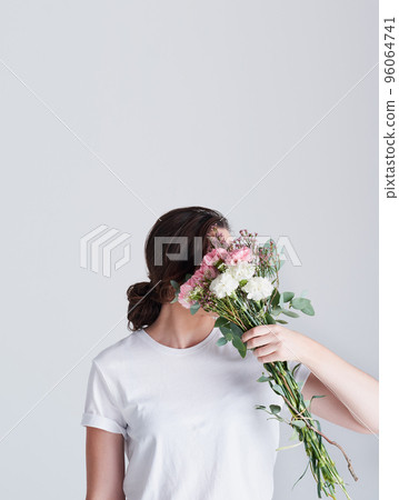 There is purity in flowers. Studio shot of an unrecognizable woman covering her face with flowers against a grey background. 96064741