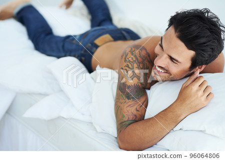 Enjoying a laugh in bed. Shot of a happy-looking young man lying on his stomach in bed. 96064806