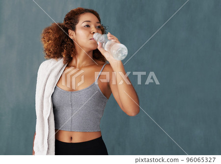 Water is an important part of any workout. Studio shot of a young woman drinking some water after yoga class against a grey background. 96065327